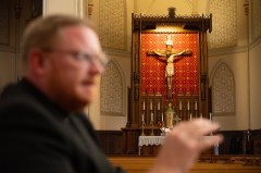 Staff Photo by Seth Carpenter / A depiction of Jesus Christ on the cross is seen as the Rev. David Carter sits at a pew inside the Basilica of Sts. Peter and Paul while speaking Oct. 6, 2026, about the Catholic Church's opposition to the death penalty.